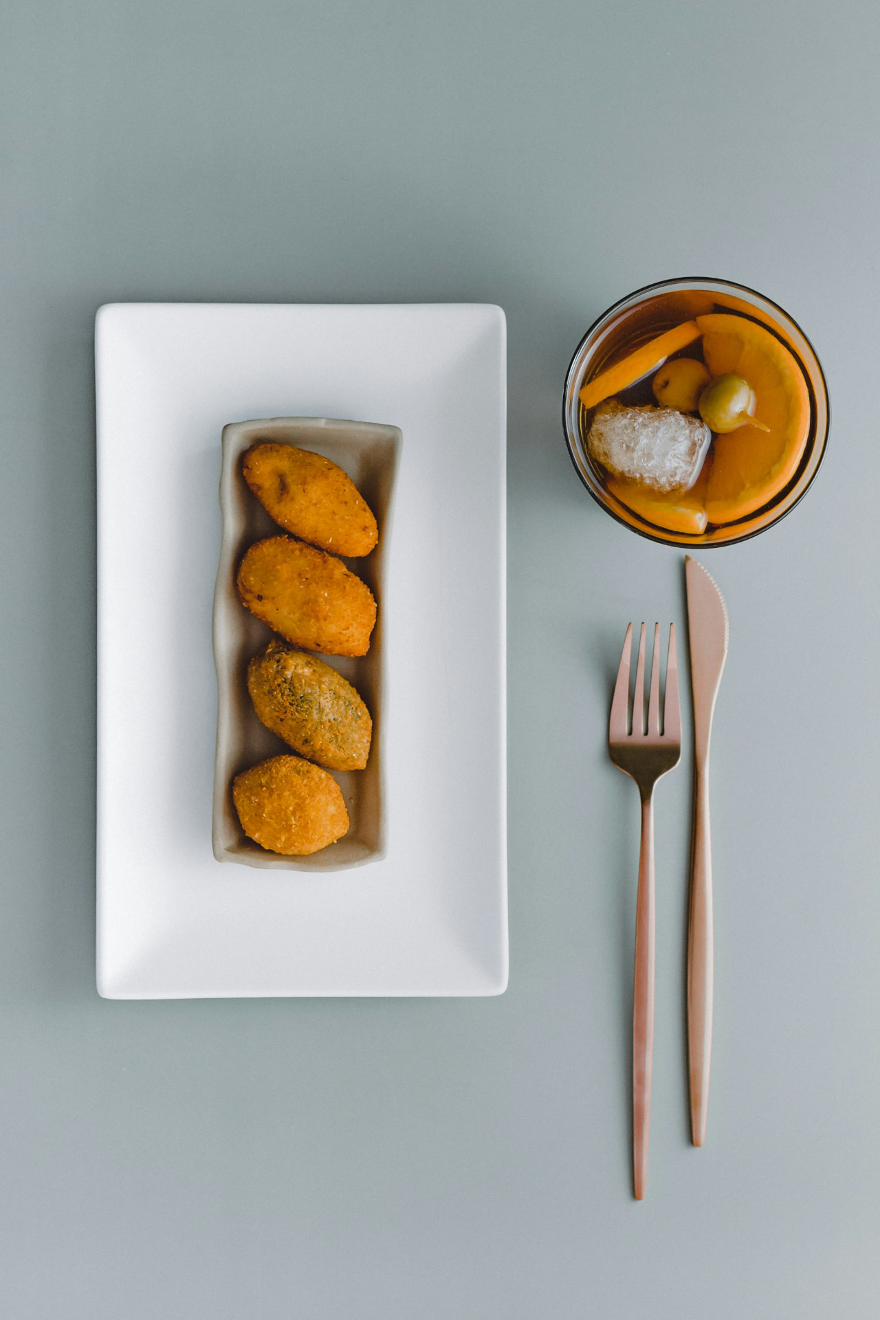 Croquetas on a white plate with a vermouth and orange