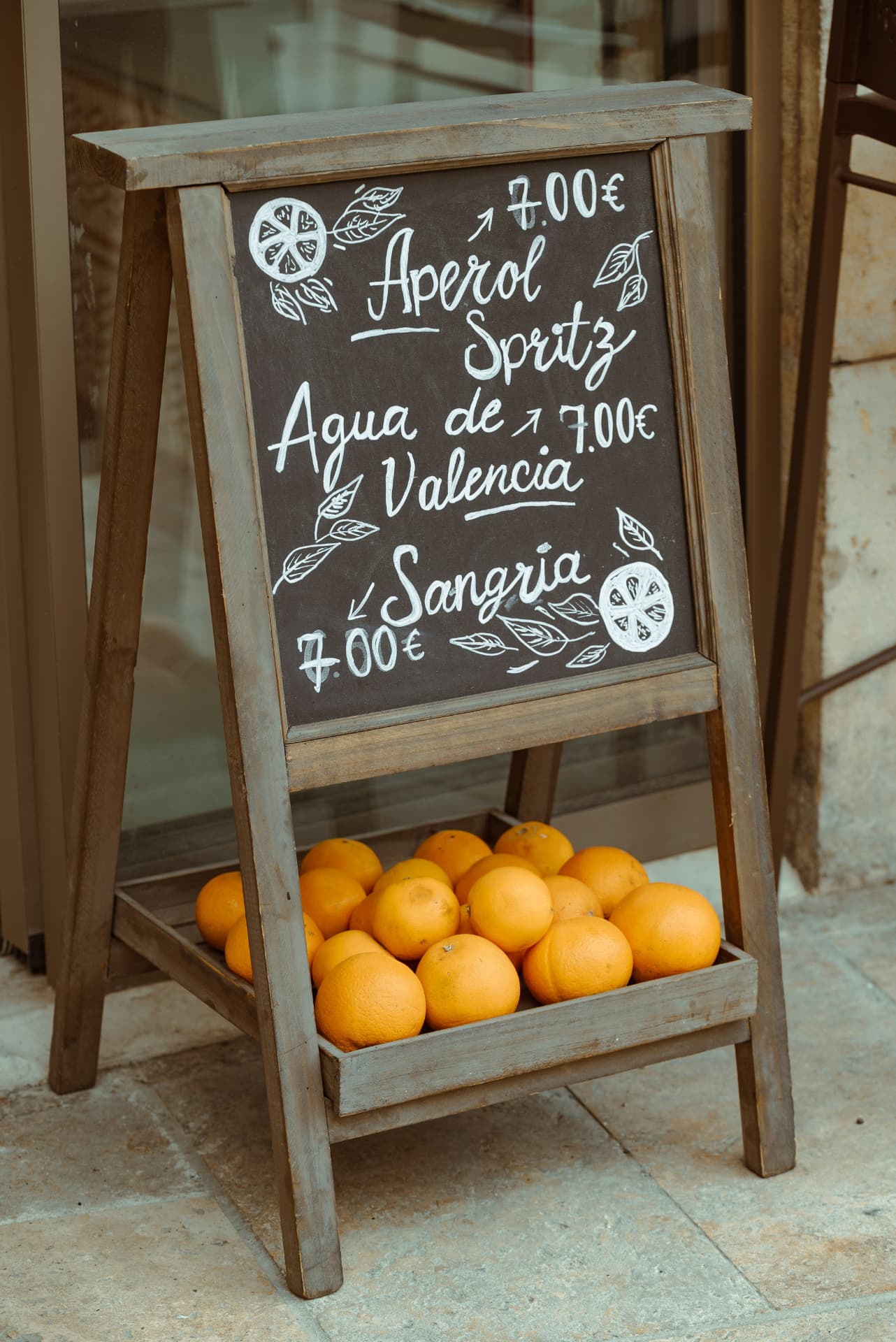 A chalkboard offering Aperol Spritz, Agua de Valencia and sangria above a crate of oranges