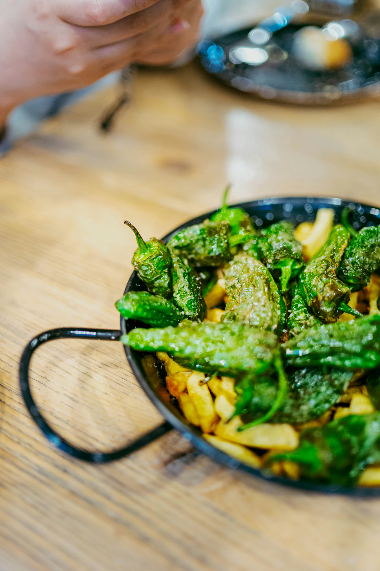Padrón peppers over fried potatoes in a small pan