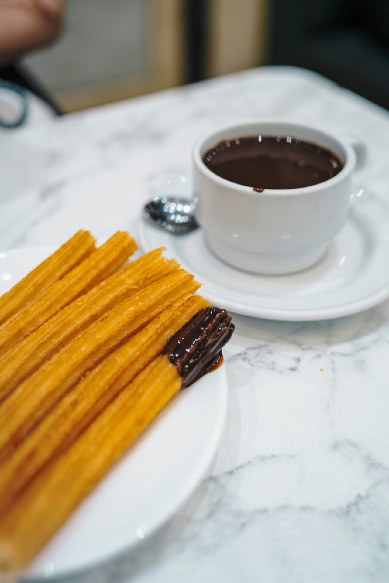Churros with a cup of thick hot chocolate on marble